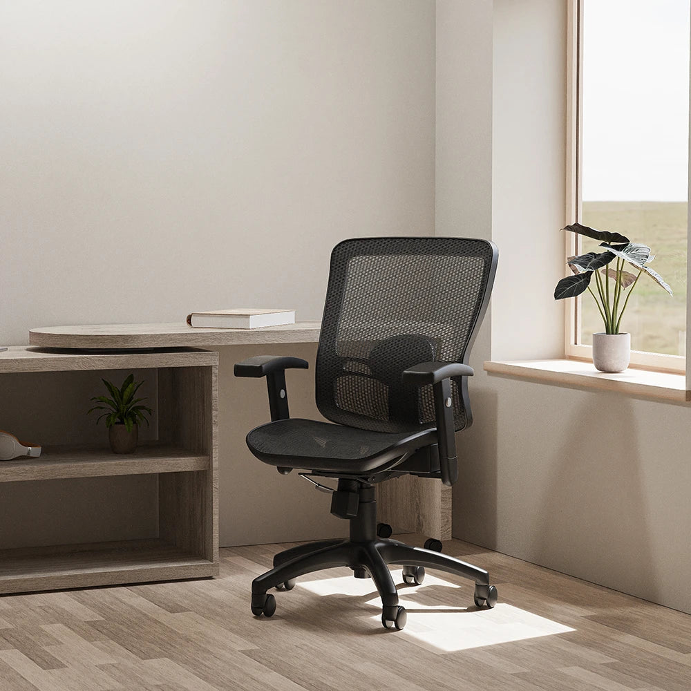Black mesh chair in a room setting with desk and and a window in the background