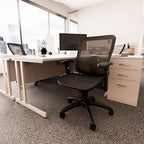 Office workstation with mesh chair, desk, pedestal and monitor with windows in a background