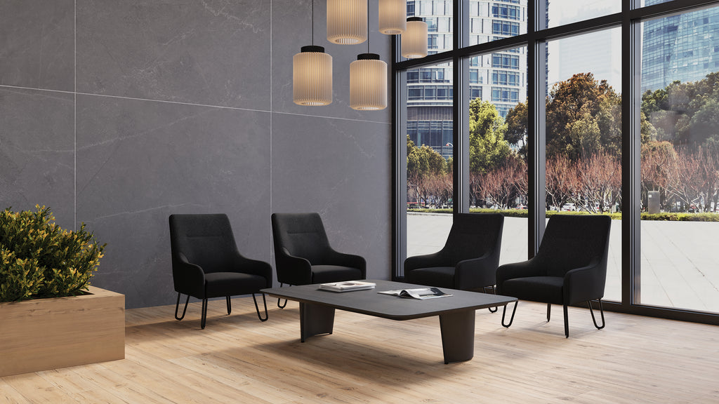 Modern office waiting area with black chairs and a coffee table near large windows.