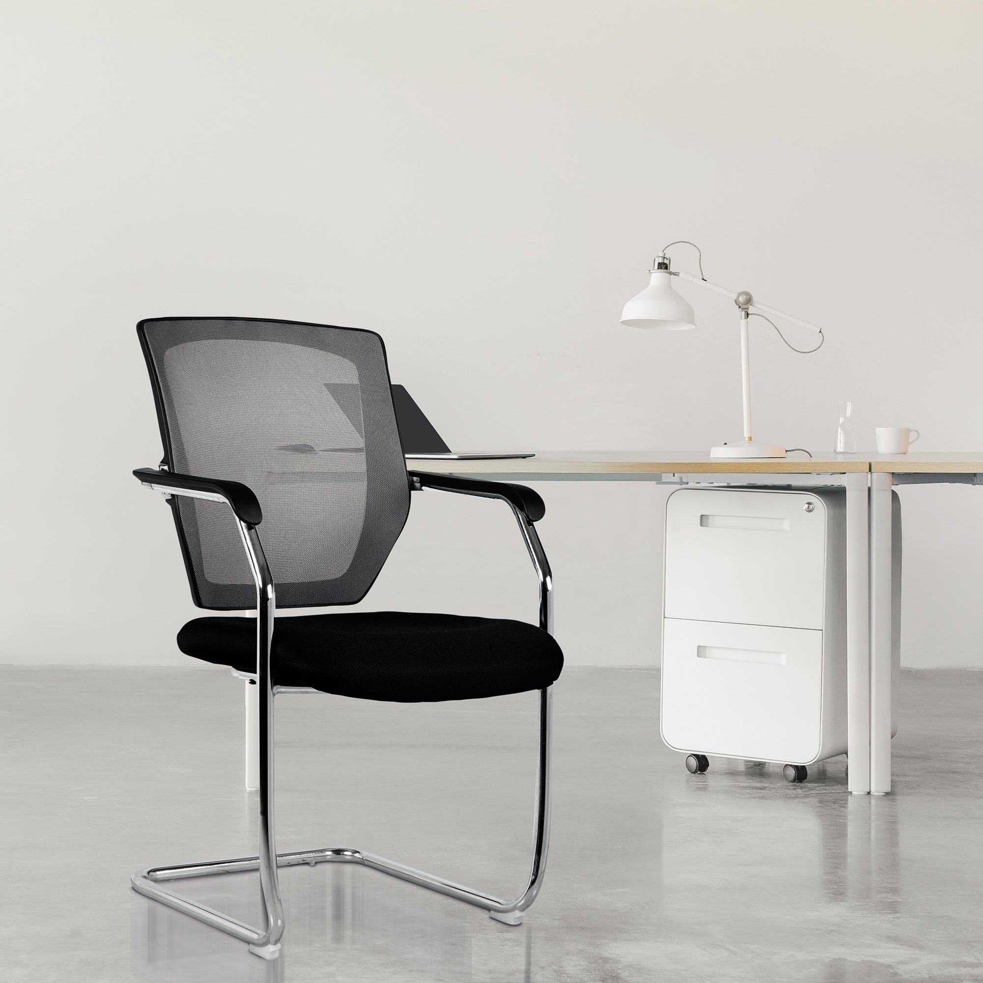 Black office chair in a minimalistic office setting with a desk and lamp.