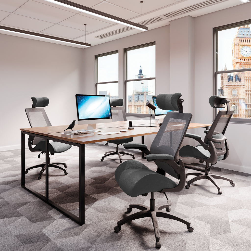 Modern office setup with desks, chairs, and computer monitors in a room with large windows.