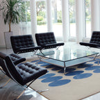 Modern living room with black chairs and a glass coffee table on a blue and beige patterned rug.