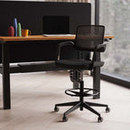 Office workstation with black high chair, desk, screen and laptop with a window in the background
