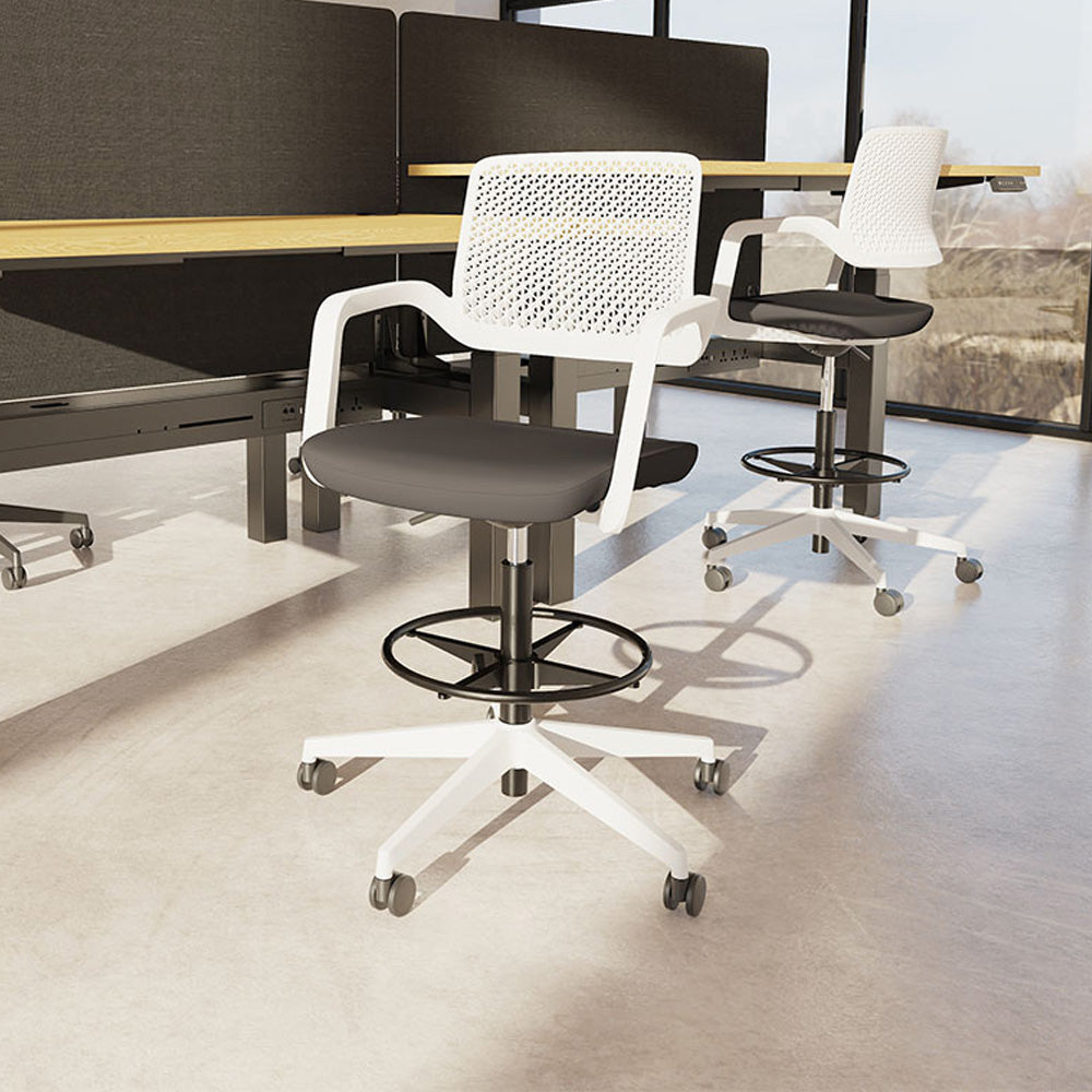 Two white high office chairs with black seats shown in an office setting with desks, screens and windows in the background