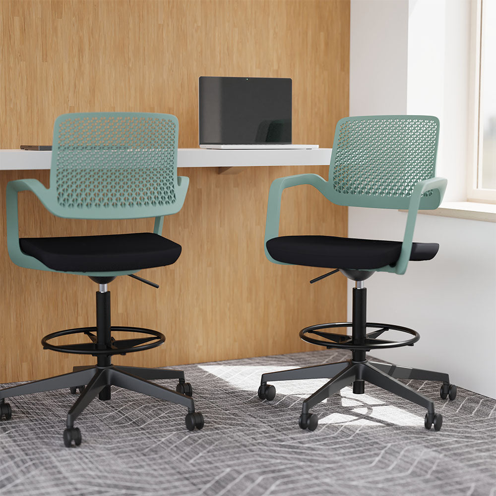 Two green and black high office chairs shown in an office setting with desk and laptop in the background