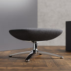 Grey footstool with a chrome frame on a wooden floor with a grey wall in a background