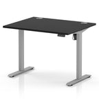 An electric height-adjustable standing desk with a black rectangular desktop and a silver metal frame, shown on a clean white background.
