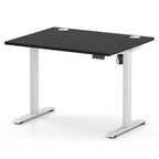 An adjustable height standing desk with a black rectangular desktop and white metal legs, shown on a clean white background.
