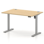 An adjustable height standing desk with a light wood grain top and a silver metal frame with T-style legs, shown on a white background.