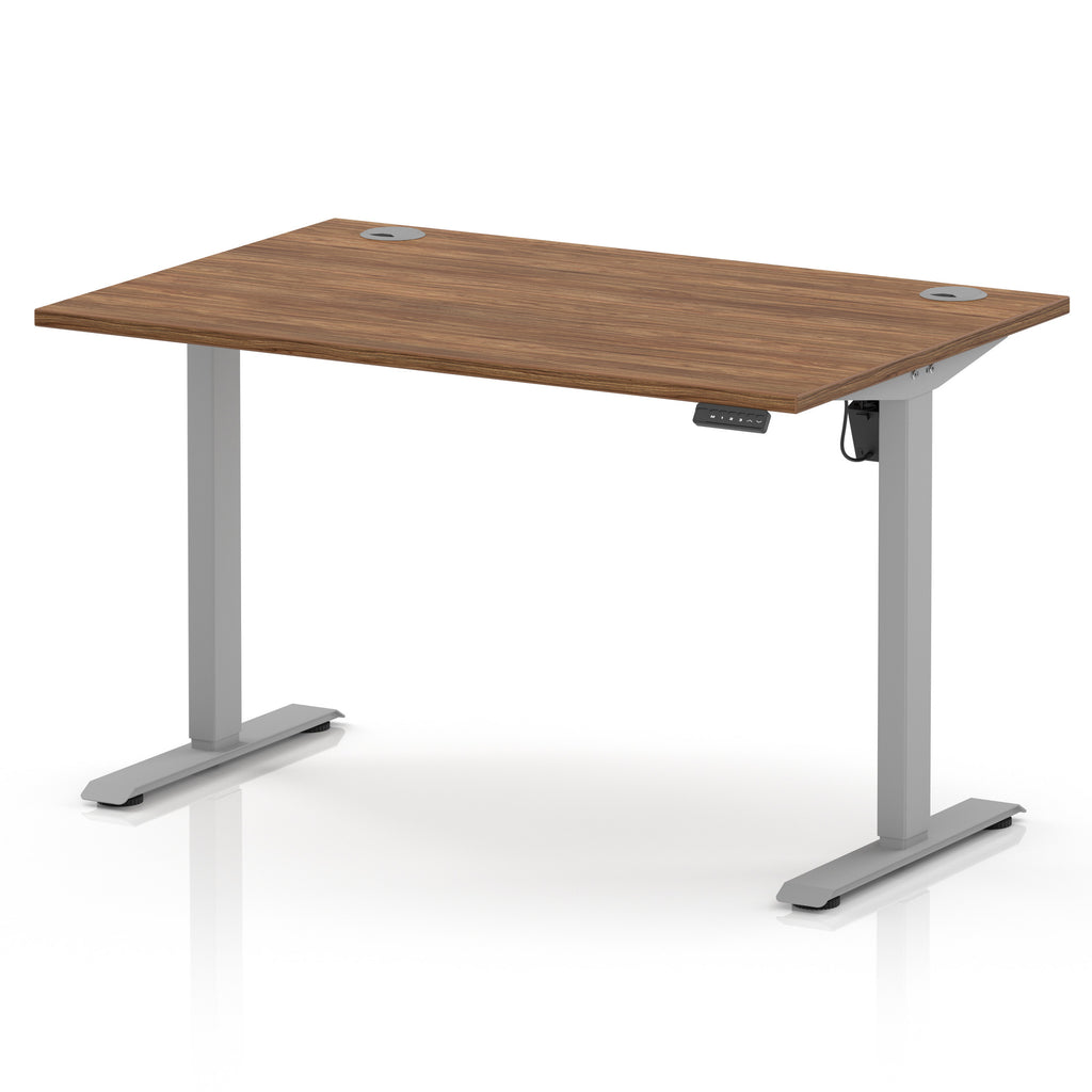An adjustable height standing desk with a medium brown wood-grain desktop and a silver metal frame with T-style legs, shown on a white background.