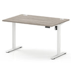 An adjustable height standing desk with a light grey wood-grain top and white metal legs, shown on a clean white background.