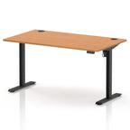An adjustable height standing desk with a light brown wood-grain desktop and black metal legs, shown on a white background with a soft reflection.