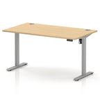 An adjustable height standing desk with a light natural wood grain top and a silver metal frame with T-style legs, shown on a white background.