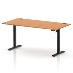An adjustable standing desk with a light brown wood-grain desktop and black metal legs, shown on a clean white background with a subtle reflection.