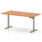 An adjustable height office desk with a light oak wood grain top and a silver metal pedestal base, shown on a clean white background.