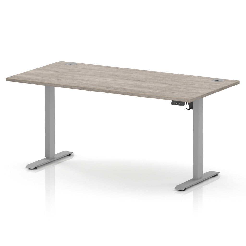 An adjustable height standing desk with a light grey wood-grain desktop and a silver metal frame with T-style legs, shown on a white background.