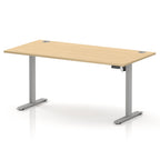 An adjustable height standing desk with a light beige wood grain top and silver metal legs, shown on a white background.