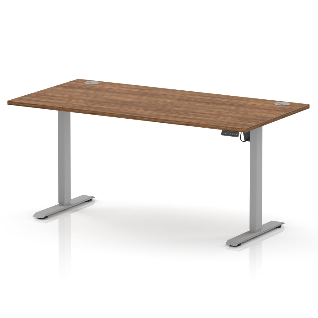 An adjustable height standing desk with a medium brown wood-grain desktop and silver metal legs, shown on a white background with a soft reflection.