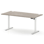 A modern height-adjustable standing desk with a light grey wood-grain top and white metal legs, shown on a clean white background.