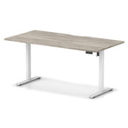 Height adjustable desk with grey wood-effect top and white frame on a white background