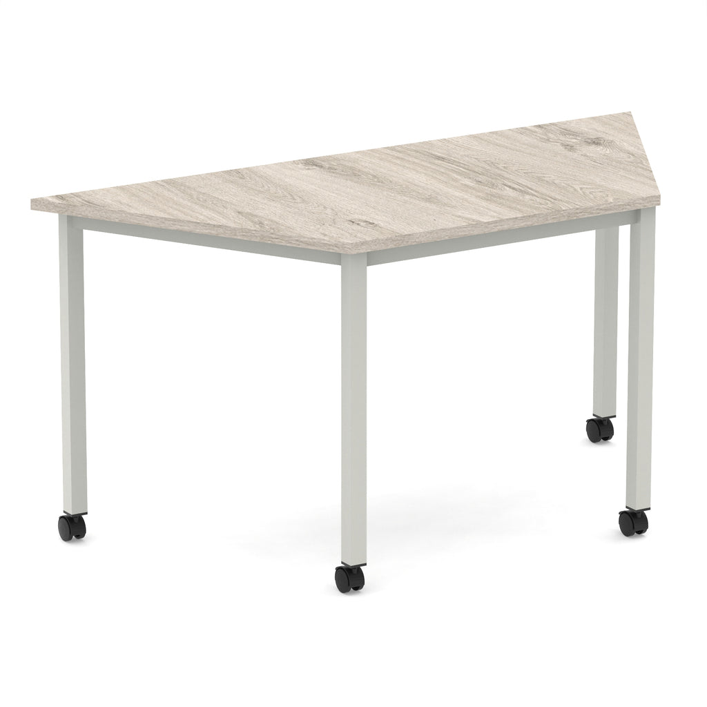 Trapezium shaped table with wood-effect top and metal frame with wheels, shown on a white background