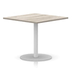 Square table with wood-effect top and white round base on a white background