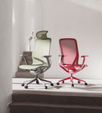 Two ergonomic mesh office chairs with adjustable armrests and five-wheel bases are displayed in a minimalist interior setting. One chair is sage green and the other is red, both on metal bases.