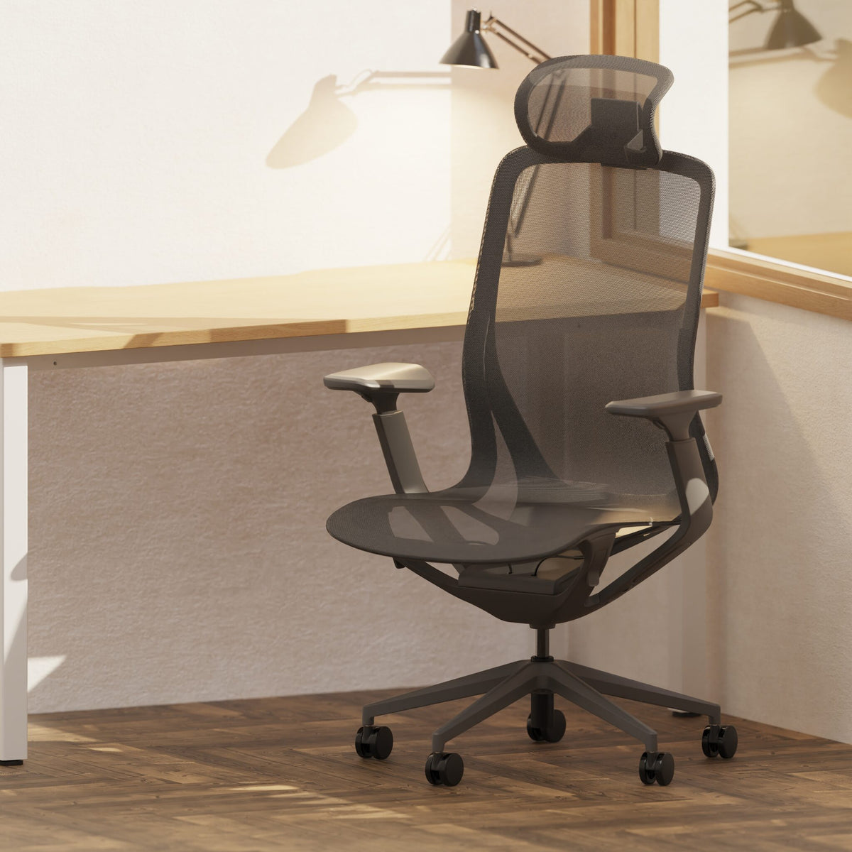 A dark grey mesh ergonomic office chair with a headrest, adjustable armrests, and a five-wheel base, positioned in front of a light wood desk in a bright office setting.