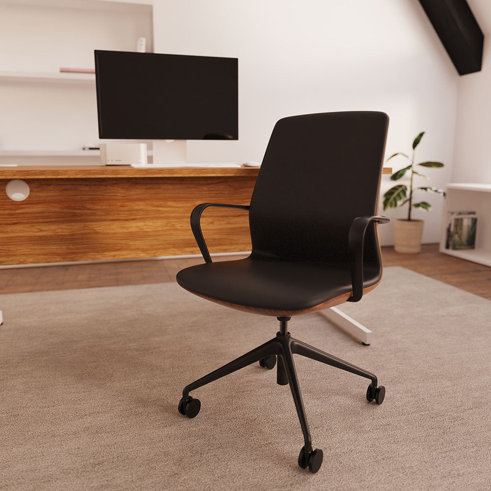 A modern black office chair with a wood-look base and black armrests, positioned on a beige carpet in a bright, contemporary home office setting.