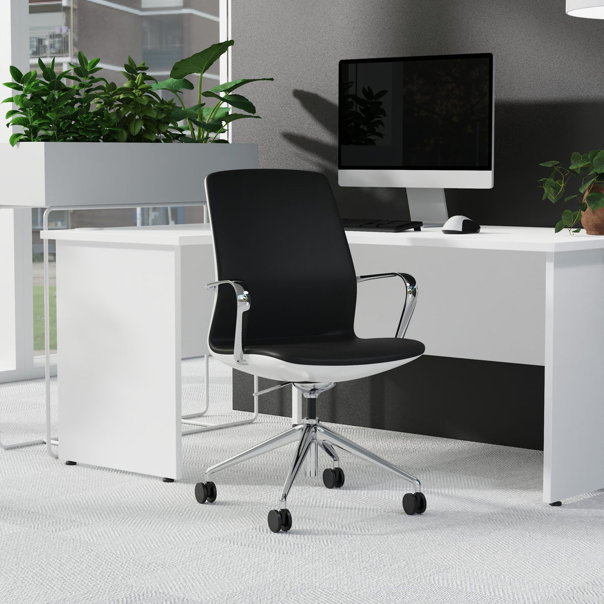 A modern black office chair with a white base and chrome armrests, positioned in front of a white desk with a computer monitor, plants, and a grey wall.