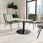 Modern green chairs around a round table in a bright room with large windows.