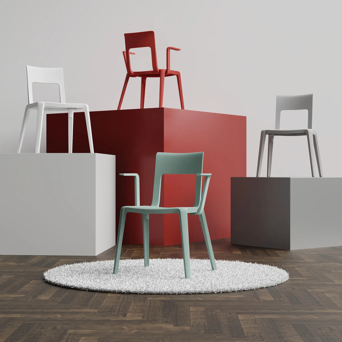 A mint green plastic chair sits on a white rug in the foreground, with four other minimalist chairs in white, red, grey, and dark grey displayed on geometric pedestals against a light grey wall.