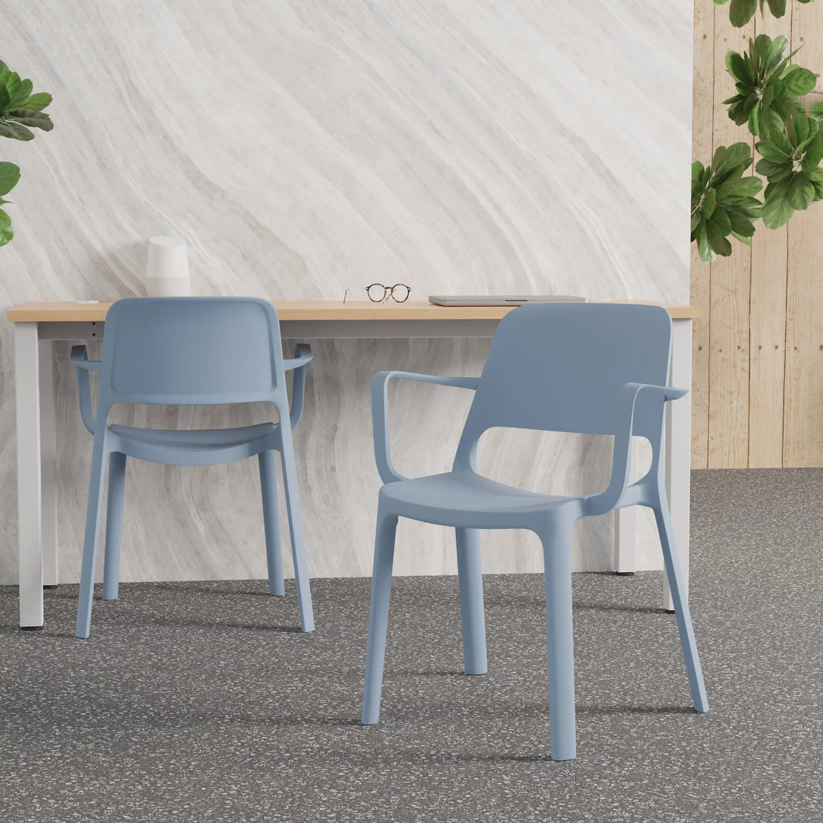 Two light blue plastic dining chairs with armrests, shown in a modern room setting with a white marble-patterned wall, a light wood table, and a speckled grey floor.