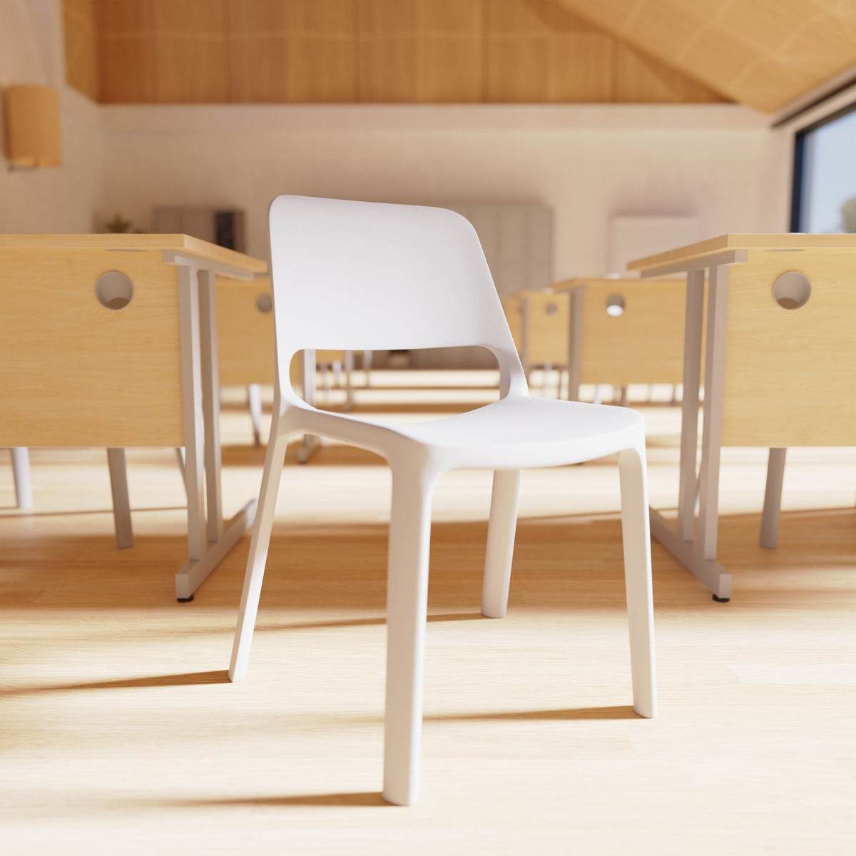 A modern white plastic chair in the foreground of a bright, sunlit classroom with light wood desks and floor.