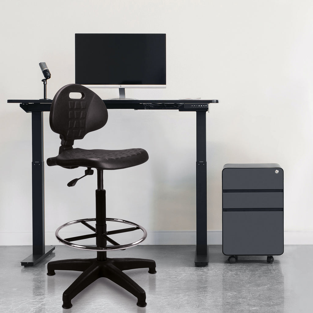 Black adjustable desk with chair and computer setup in a minimalistic room.