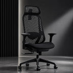 A black mesh ergonomic office chair with a high back, triangular patterned backrest, adjustable armrests, and a five-wheel base, set against a dark gray studio background with dramatic lighting.