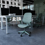 A blue ergonomic office chair with a mesh back and five-star wheeled base, positioned in front of a desk with multiple computer monitors in a modern office setting.