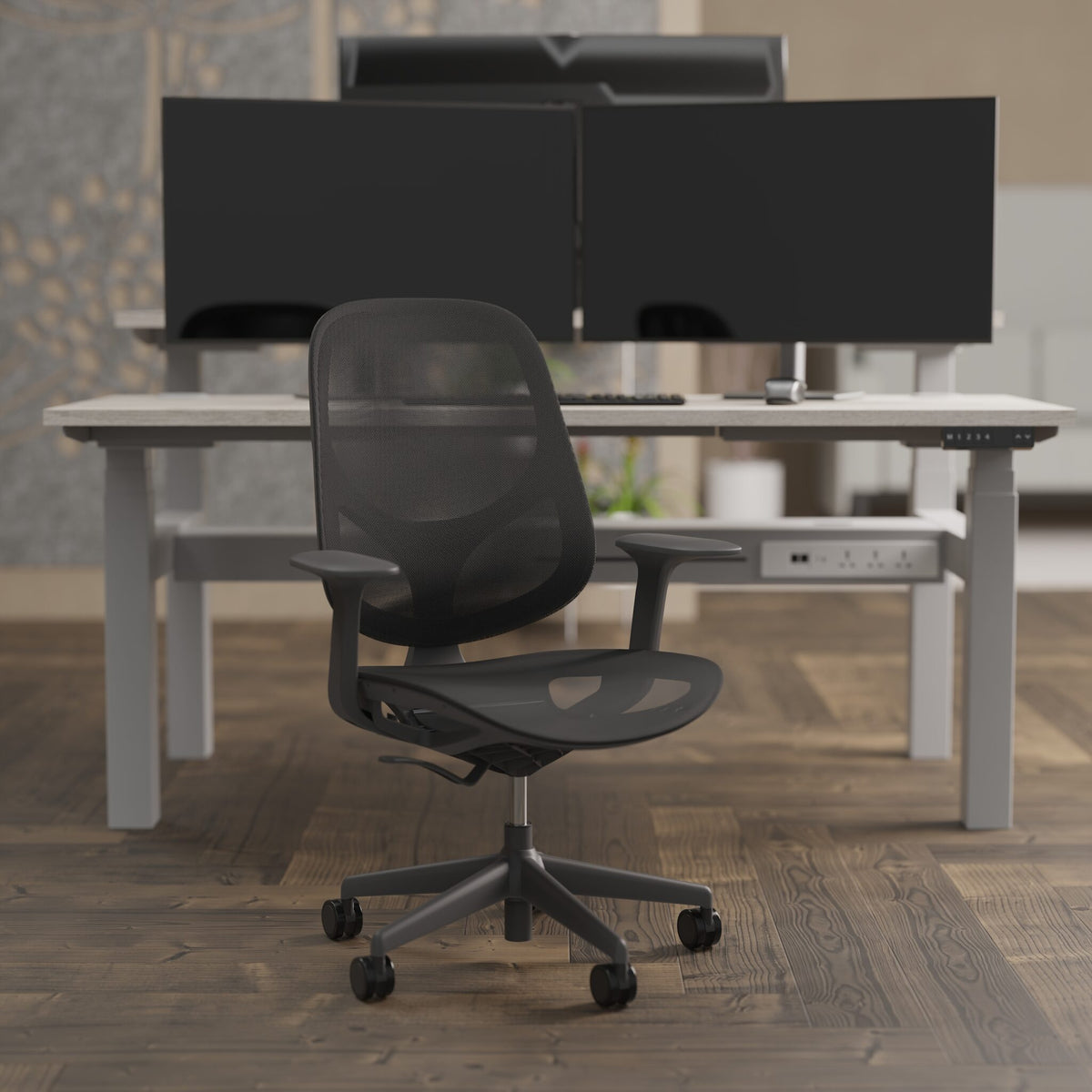 A modern black mesh office chair with a five-star wheeled base, positioned in front of a light grey standing desk with dual computer monitors in a home office setting.