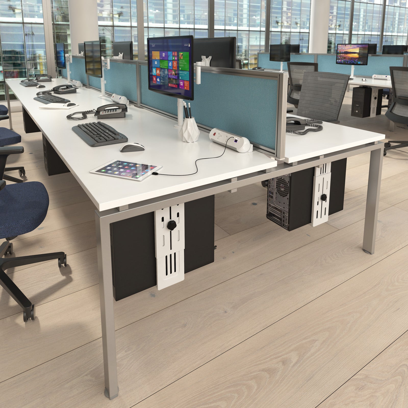 A modern office desk setup with a white desktop, silver metal frame, light blue privacy dividers, and black under-desk storage cabinets, shown in a bright office environment with office chairs and computer monitors.