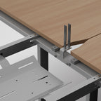 Close-up of a desk frame showing a light wood desktop, metal support brackets, and a gray desk base against a white background.