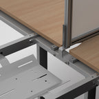 Close-up of a desk frame with light wood grain desktop surfaces, a light grey divider panel, and a grey metal desk base on a clean white background.
