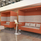 Modern office lounge with orange and grey seating area and a standing desk.