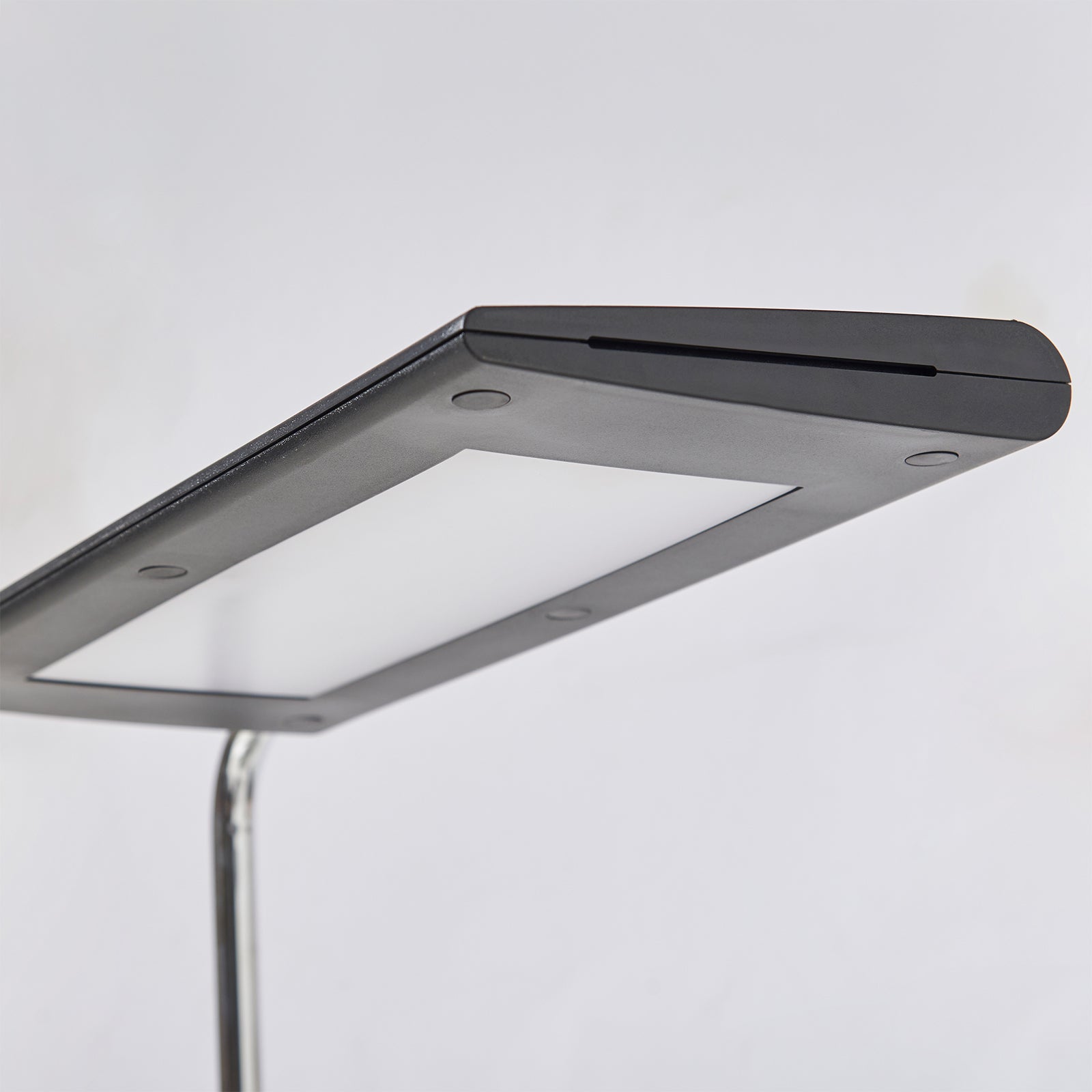 A close-up of a modern rectangular lamp with a matte black top cover, a silver metallic frame shown against a plain light grey background.