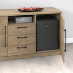 A light wood storage cabinet with three drawers, open shelves, and a door pulled open to reveal a small black refrigerator inside. A tray of red apples and a stack of magazines sit on top.
