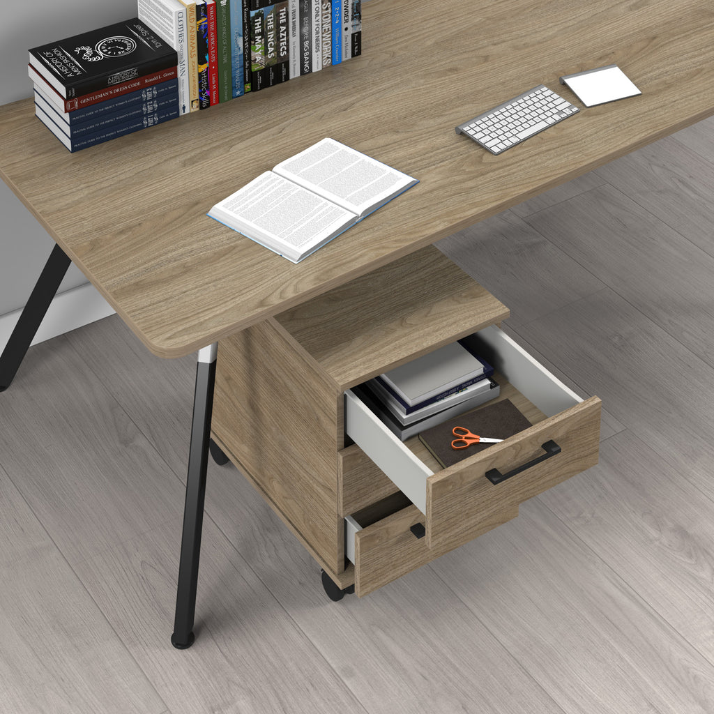A wooden desk with a drawer unit and black metal legs, shown on a grey wood-look floor with books, an open book, a keyboard, and a card on top.