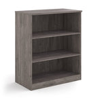 A three-tier bookcase with a grey wood-effect finish, shown from a three-quarter angle on a solid white background.