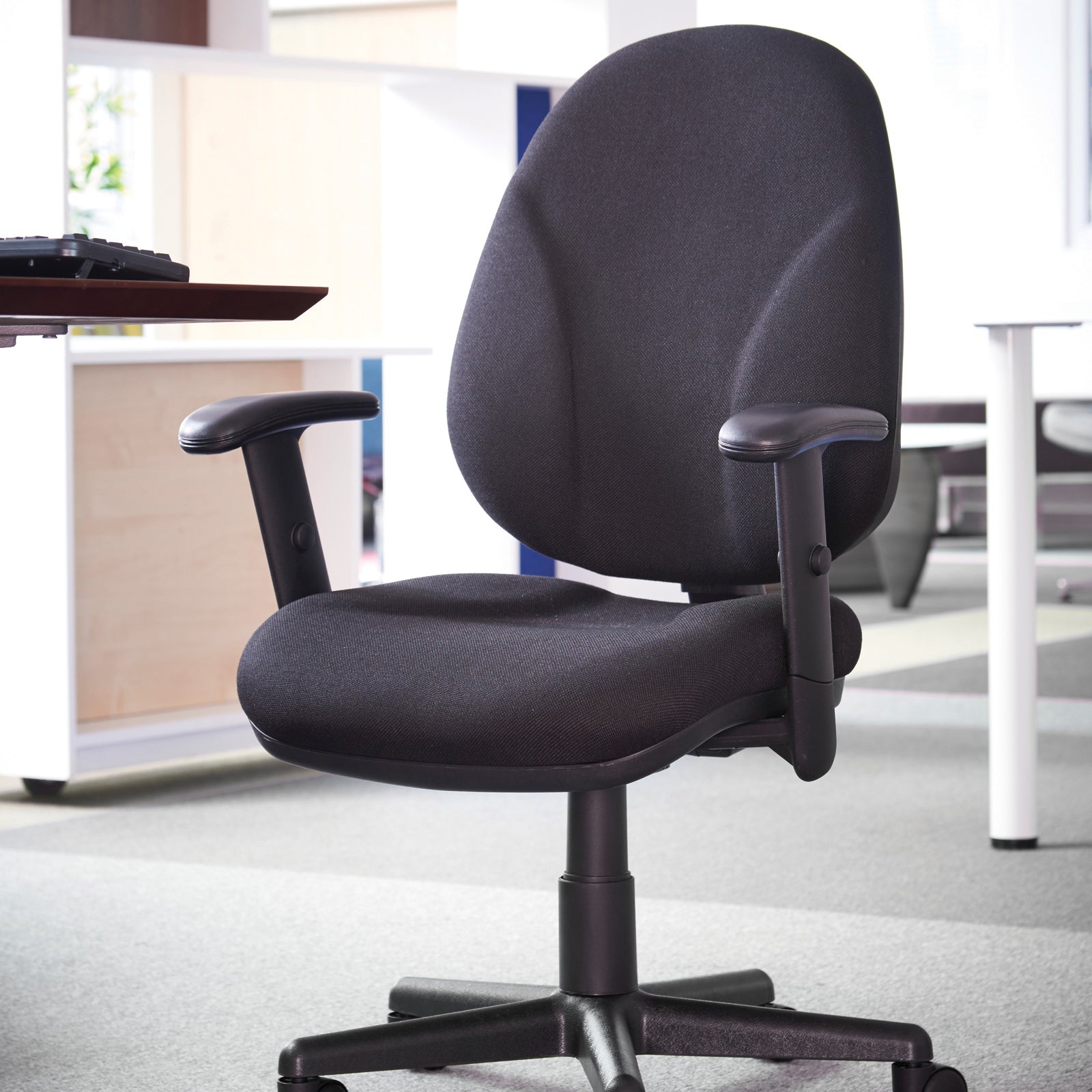 Black office chair in an office setting with a desk and computer in the background.