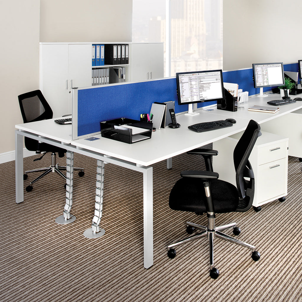 Modular bench desk system with white desktops, blue fabric desk-mounted privacy screens, integrated cable management spines, and white metal legs, shown in a modern open-plan office setting.