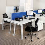 Modular bench desk system with white desktops, blue fabric desk-mounted privacy screens, integrated cable management spines, and white metal legs, shown in a modern open-plan office setting.