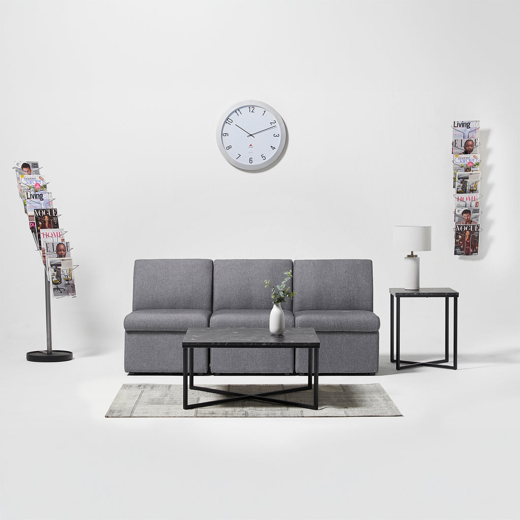 Gray sofa in a living room with a clock on the wall and magazine holders.